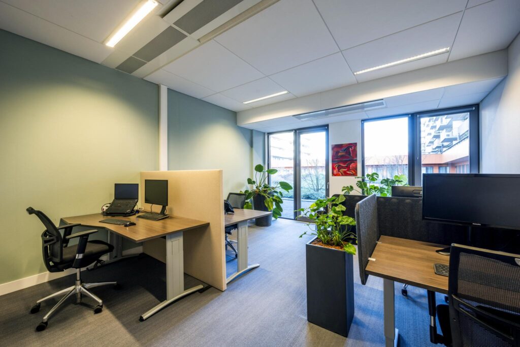 Modern kantoorinterieur aan de Laan van de Helende Meesters met werkplekken, bureaustoelen, computers en veel groen.